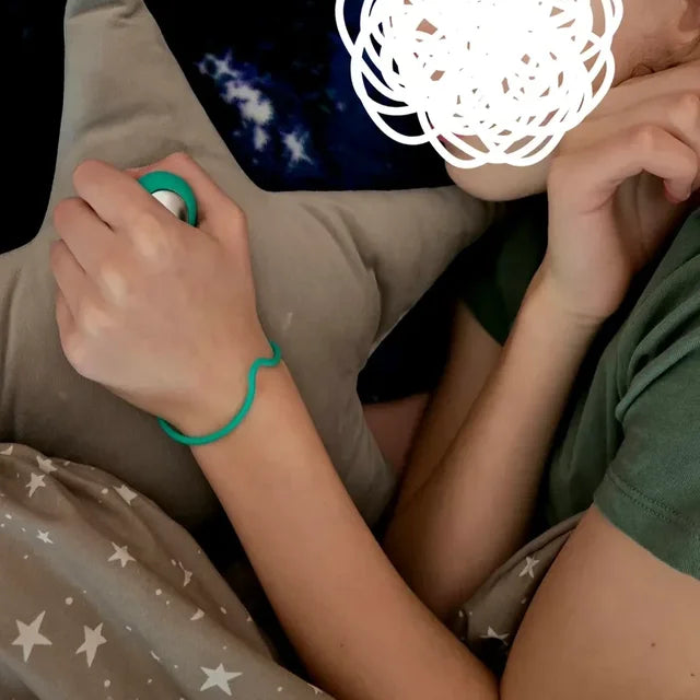 Une enfant allongée tient son CalmKid turquoise, la dragonne au poignet.
