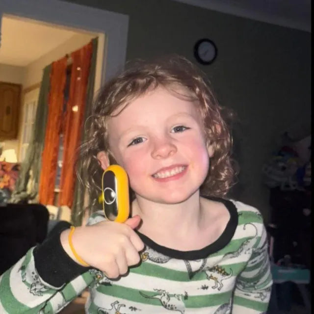 Un petit garçon aux cheveux bouclés, en pyjama, sourit et lève le pouce avec son CalmKid.