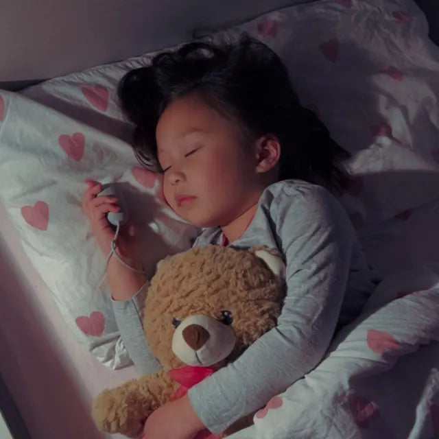 Une petite fille endormie avec son nounours, son CalmKid dans la main.