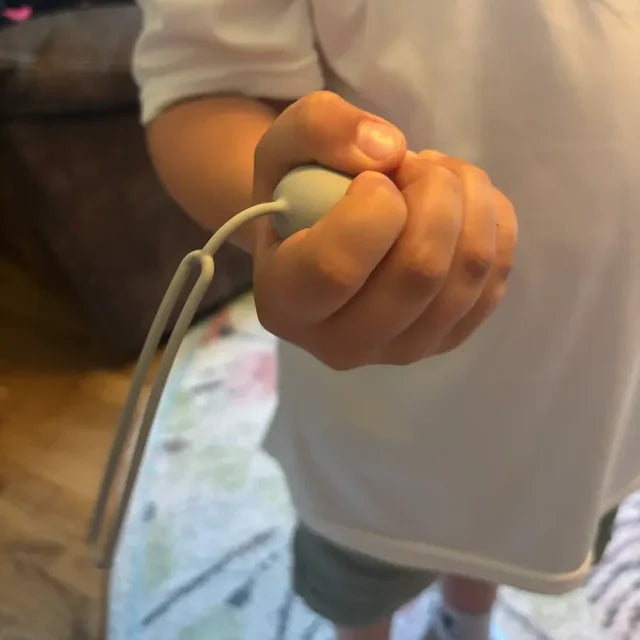 Un enfant serre son CalmKid gris dans le poing, la dragonne pendante.
