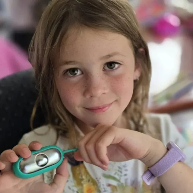 Une petite fille souriante montre son CalmKid turquoise dans sa main.