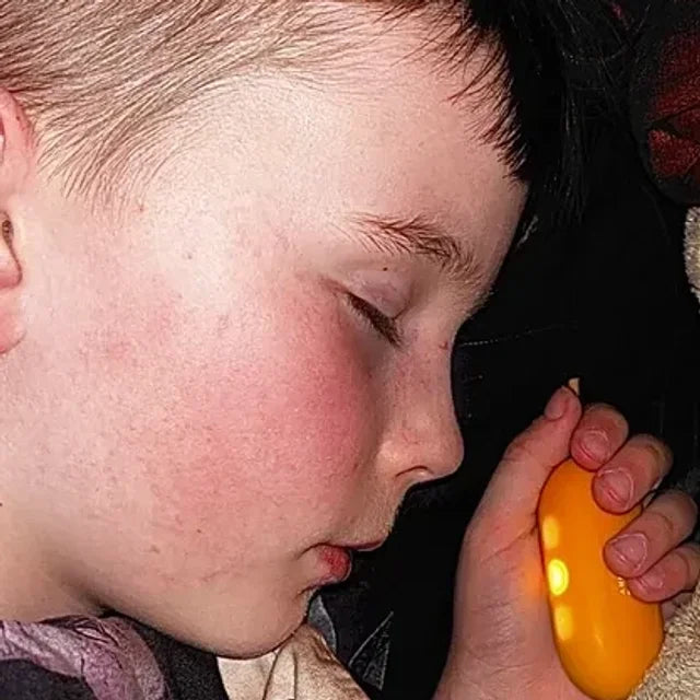 Un garçon endormi, son CalmKid orange dans la main.