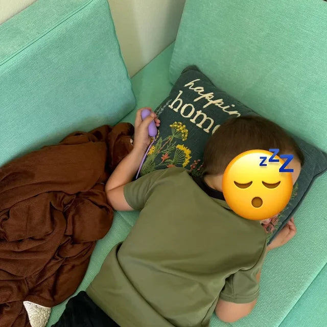 Un petit garçon endormi sur le canapé, son CalmKid violet dans la main.