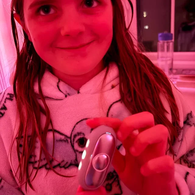 Une fille en pyjama montre son CalmKid avant de dormir, dans la lumière rose de sa veilleuse.