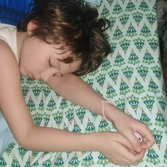 Un garçon endormi, son CalmKid rose dans les mains, la dragonne au poignet.