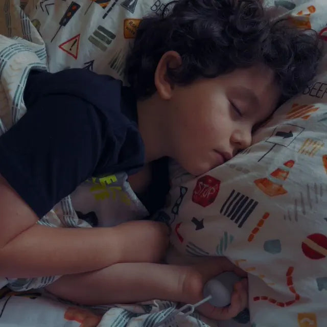 Un petit garçon endormi dans son lit, son CalmKid dans la main.