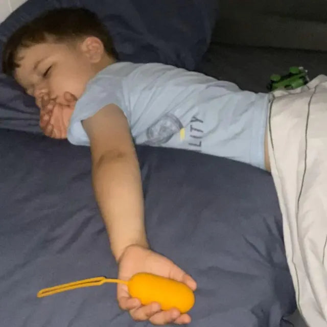 Un petit garçon endormi, son CalmKid orange dans la main, la dragonne posée sur la couette.
