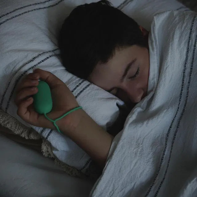 Un garçon endormi sous la couette, son CalmKid vert dans la main, la dragonne au poignet.