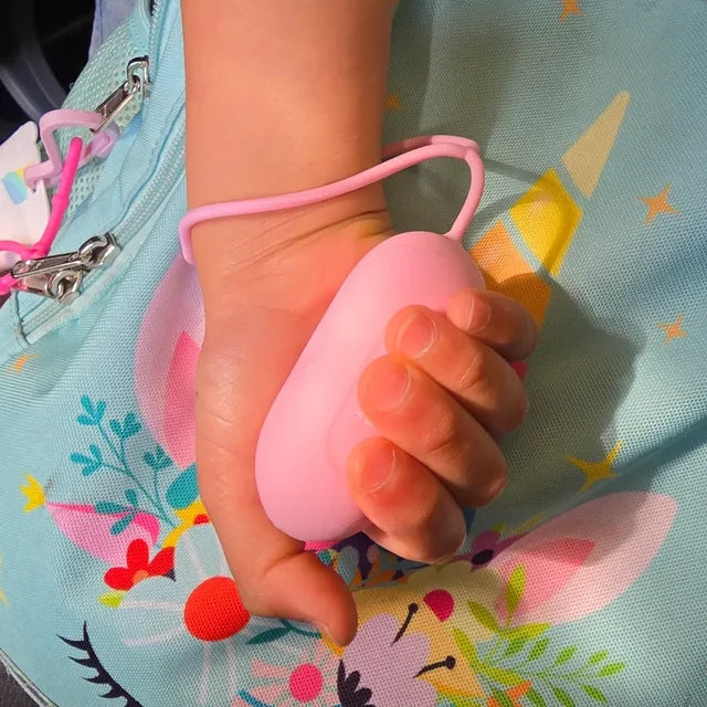 Une main d'enfant serre un CalmKid rose, la dragonne au poignet, sur son sac à dos.